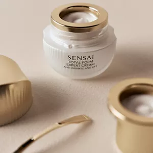 Opened Total Form Expert Cream jar showcasing the texture next to its refill, top and spatula on neutral surface